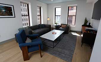 Levi Level Rockefeller Suite sitting area with couch, chairs, coffee table, TV and natural light from windows